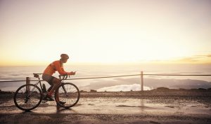 Full length shot of a young woman sending a text while cycling in the mountains